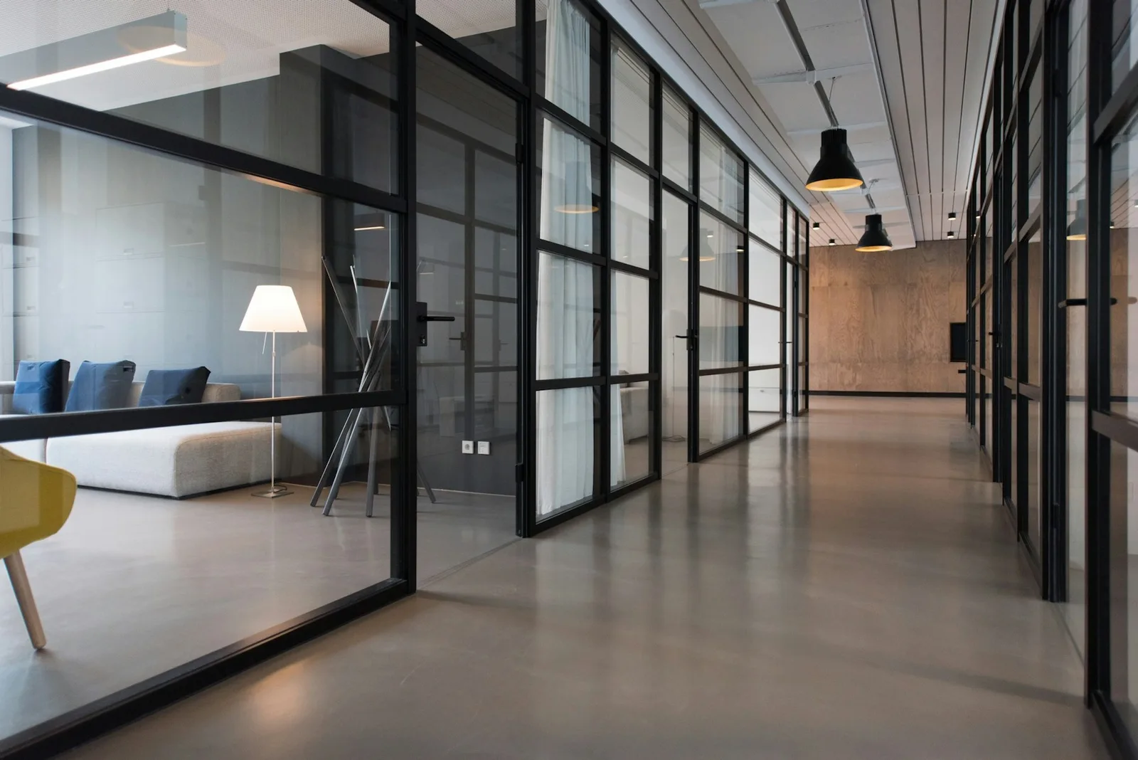 Glass-walled commercial office corridor with meeting rooms and warm pendant lights