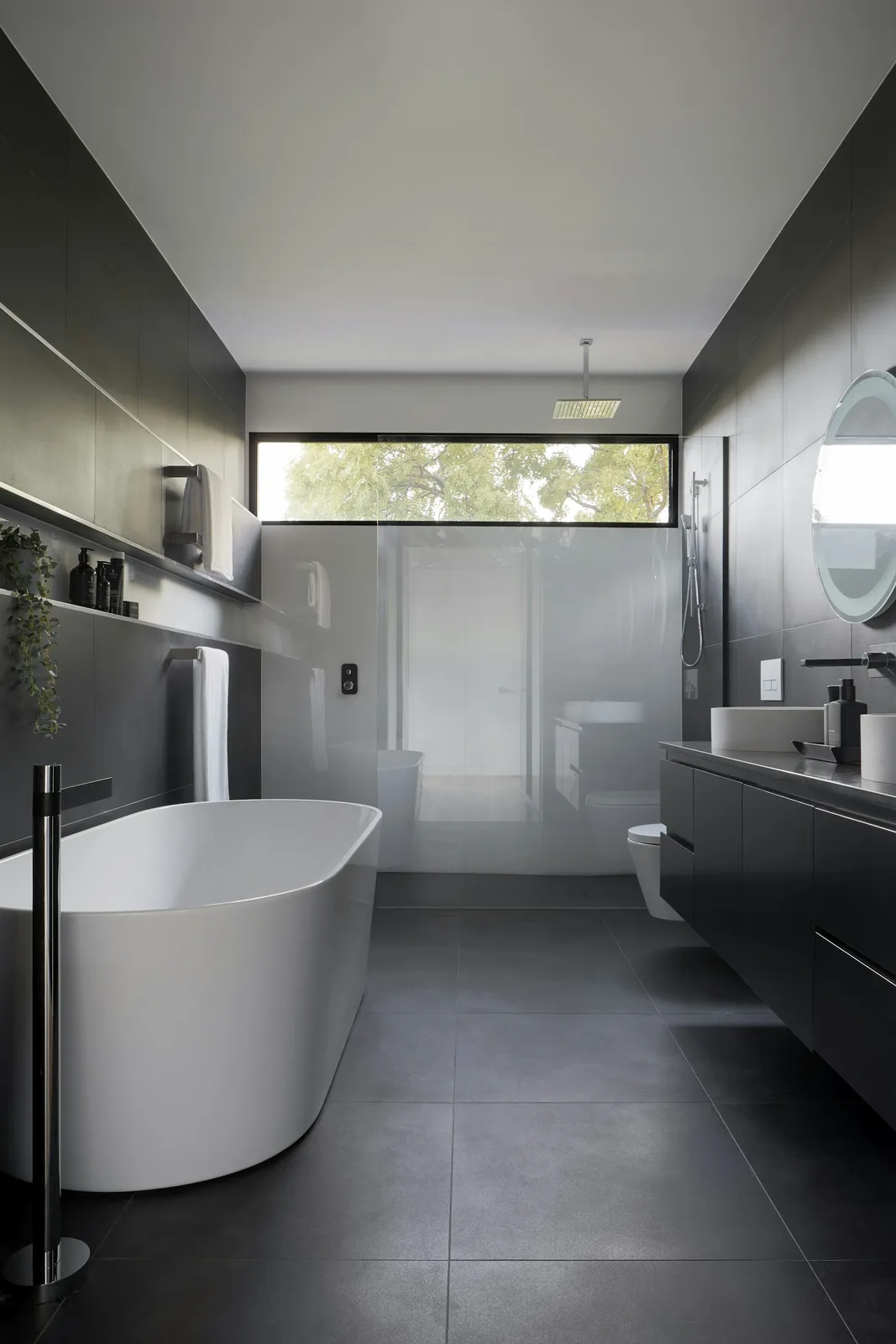 Sunlit bathroom with a freestanding tub, dark tile, and a simple wood vanity