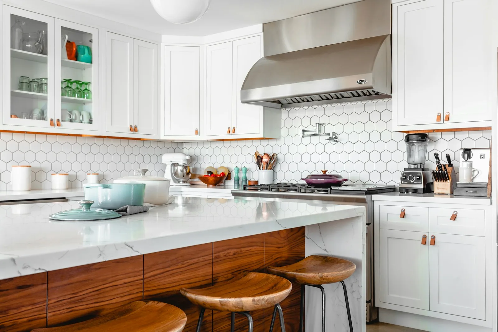 Bright kitchen with white cabinetry, wood stools, and a clean stone worktop